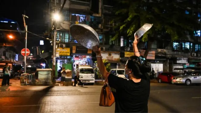 A woman clatters pans to make noise after calls for protest went out on social media in Yangon