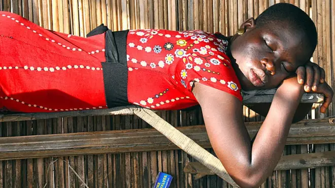 Une jeune femme dort à l'ombre, à l'abri du soleil de l'après-midi. Elle travaille dans un bar au bord de la route à côté de l'atelier de mécanique à Gadome, sur la route principale au nord-ouest de Cotonou au Bénin.