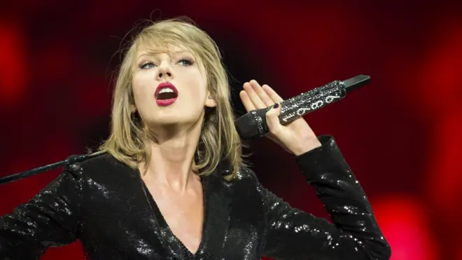 Taylor Swift holds microphone on-stage while performing