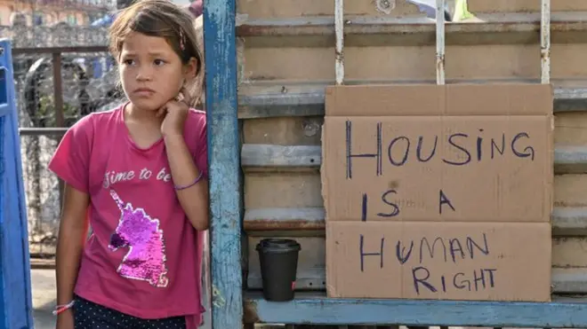 "La vivienda es un derecho humano", reza el cartel junto al que está está niña refugiada en Grecia.