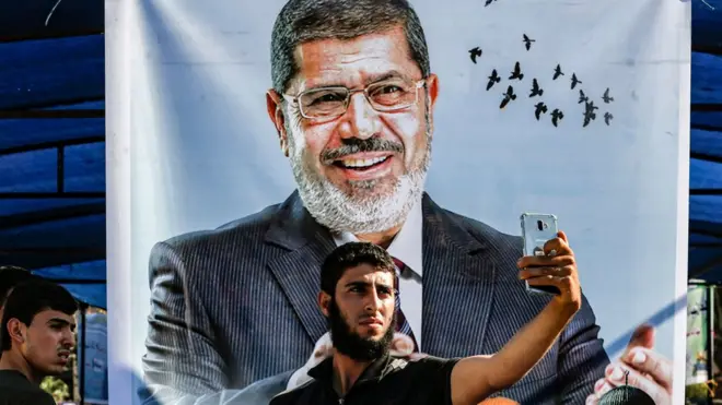 Seorang pemuda Palestina mengambil foto dengan latar belakang spanduk Muhammad Mursi di kawasan Jalur Gaza selatan.