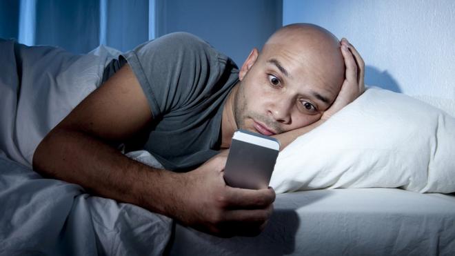Hombre acostado en la cama revisando su celular