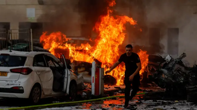 Un homme court sur une route alors que le feu brûle après que des roquettes ont été lancées depuis la bande de Gaza, à Ashkelon, Israël Octobre