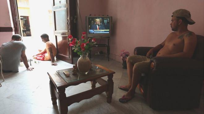 Un cubano ve el discurso de Trump desde el televisor de su casa mientras dos jóvenes juegan ajedrez en el portal.