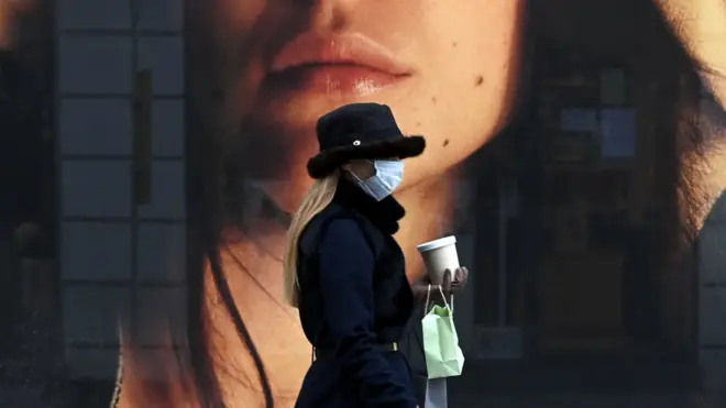 A woman wearing a protective mask walks past a store window in the city of Munich