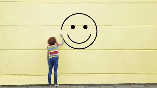 Child draws a smiling face on a yellow wall