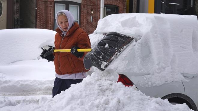امرأة تزيح الثلوج التي طمرت سيارتها