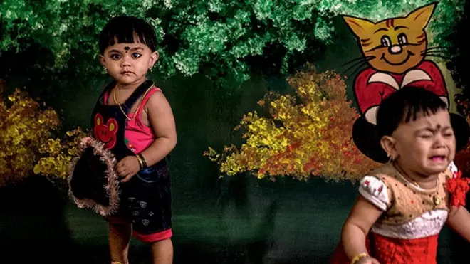 새가 날아가는 그림을 배경으로 쌍둥이 아기 중 한 명은 카메라를 응시하고, 다른 한 명은 울고 있다