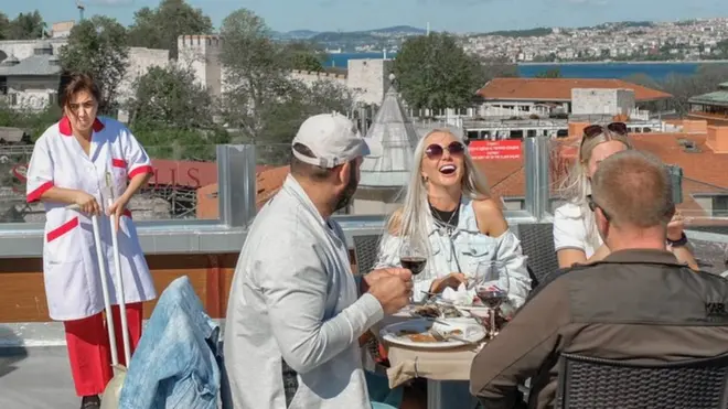 مجموعة من السياح يتناولون وجبة في اسطنبول بينما تقف عاملة نظافة على مقربة منهم