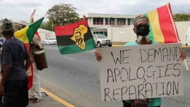 متظاهر يحمل لافتة خلال مسيرة يطالب ملكة بريطانيا بتقديم اعتذار وتعويضات عن العبودية، قبل زيارة دوق ودوقة كامبريدج إلى جامايكا كجزء من جولتهما في منطقة البحر الكاريبي، خارج المفوضية البريطانية العليا في كينغستون ، جامايكا 22 مارس 2022.