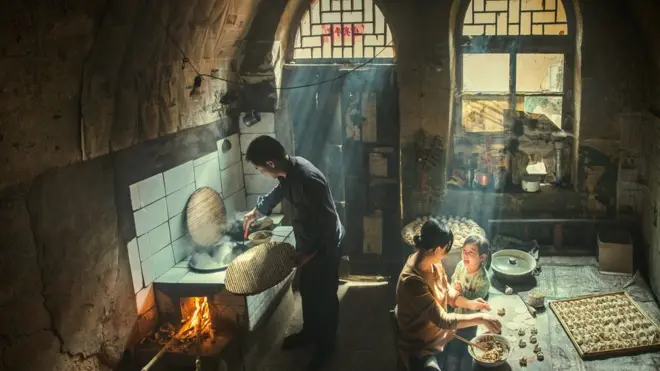 Family preparing food indoors, with rays of sunlight shining through the windows