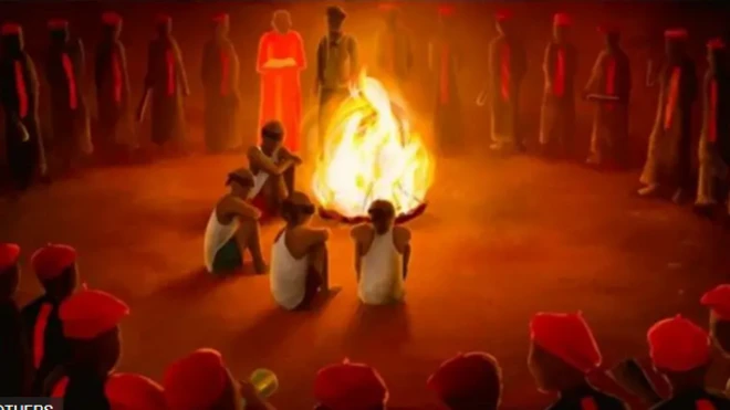 Awọn ọmọ ẹgbẹ okunkun to yika ina nla kan, wọn joko sori ilẹ, de fila pupa