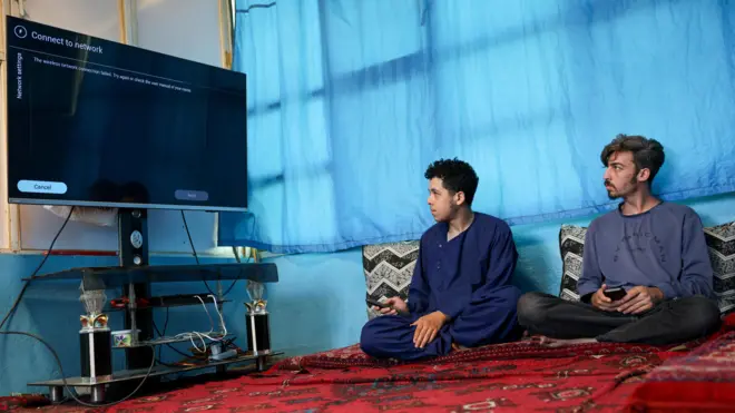 Mężczyźni próbują podłączyć telewizor smart do internetu, podczas gdy w całym kraju panuje przerwa w dostawie usług telekomunikacyjnych.