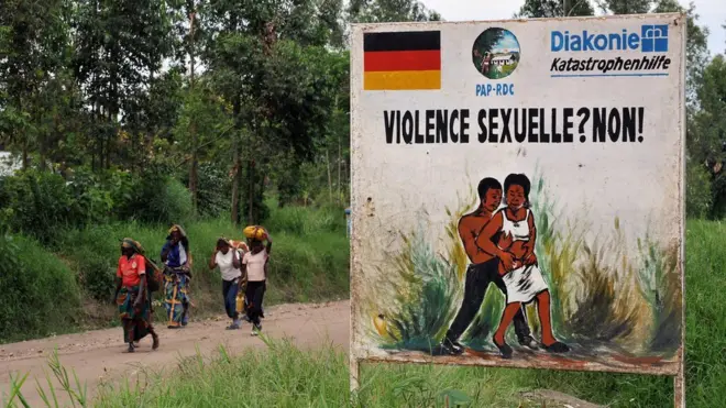 Congolese women walk past a sign opposing sexual violence on December 4, 2008 in Nyamilima, in Nord-Kivu, in the east of the Democratic Republic of Congo (DRC).