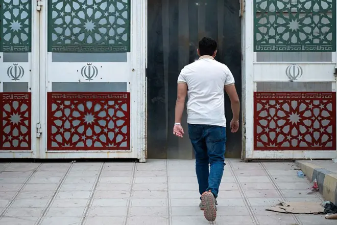 تصویر مردی از پشت سر که به سمت درگاهی منقش به پرچم جمهوری اسلامی ایران میرود