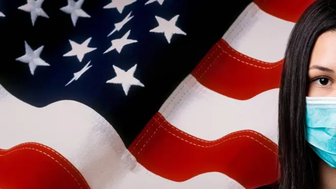 Stock photo showing an Asian woman wearing a mask, in front of a US flag