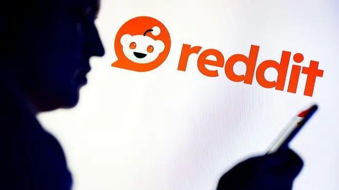 Силуэт мужчины с мобильным телефоном в руке на фоне логотипа Reddit.