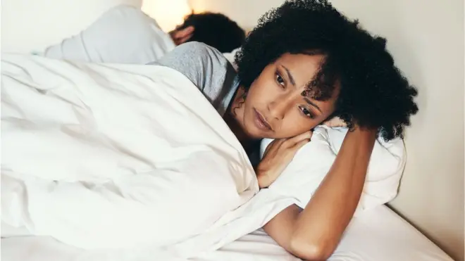 Une femme, le dos tourné à un homme, est pensive couchée sur son lit