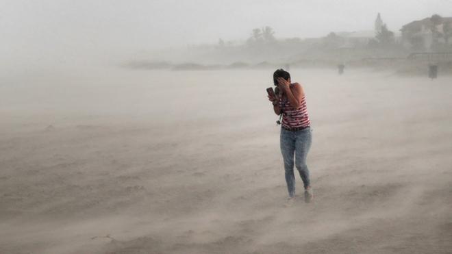 A woman seeks cover from wind, blowing sand and rain whipped up by Hurricane Dorian as she walks on the beach on September 2, 2019 in Cocoa Beach, Florida.