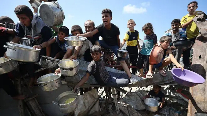 صورة بتاريخ 3 سبتمبر/أيلول في مدينة غزة، حيث أُُعلنت المجاعة ويظهر فلسطينيون يحملون أواني وأوعيةً، ويشكلون حشداً لتلقي مساعدات غذائية مقدمة من جمعية خيرية في المدينة.