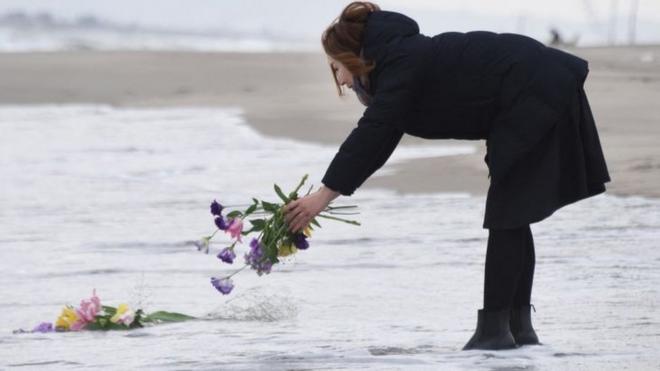 日本仙台海边一位女士将鲜花抛进海中悼念东日本大地震与海啸死者（11/3/2016）