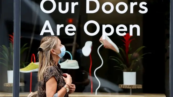 FILE PHOTO: A woman walks past a shop window near Covent Garden, wearing a protective mask under the new rules that enforce wearing face coverings in enclosed public spaces, amid the coronavirus disease (COVID-19) outbreak, in central London, Britain July 24, 2020
