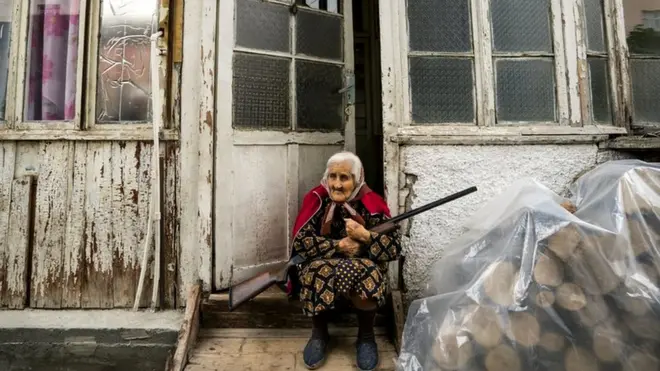 Old woman stands in the entrance of her home with a rifle during the shelling of Stepanakert city