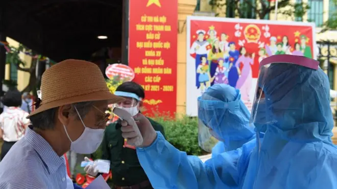 Kiểm tra thân nhiệt cử tri tại một điểm bỏ phiếu ở Hà Nội hôm 23/5/2021