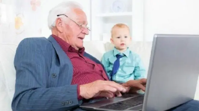 رجل كبير يستخدم كمبيوتر محمول وبجانبه طفل صغير