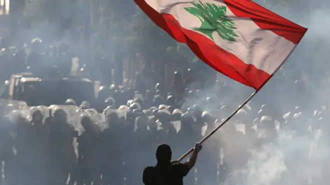 متظاهر يلوح بعلم لبنان في مواجهة قوات الشرطة
