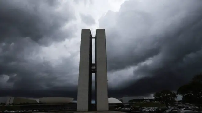 Prédios do Congresso Nacional sob nuvens pesadas em Brasília; representantes do Executivo e da Câmara dizem que revisar teto pode agravar a crise