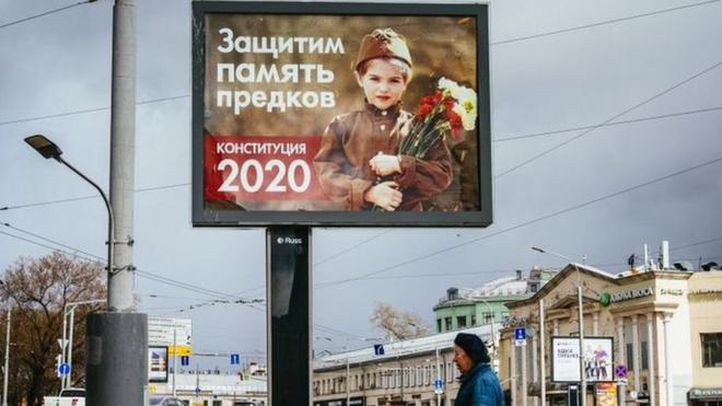 امرأة تمرّ على لوحة إعلانات عليها صورة طفلة ترتدي الزي الرسمي للجيش