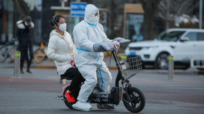 北京街頭一位防疫人員騎著電動摩托車載著一位女子走過（30/11/2022）