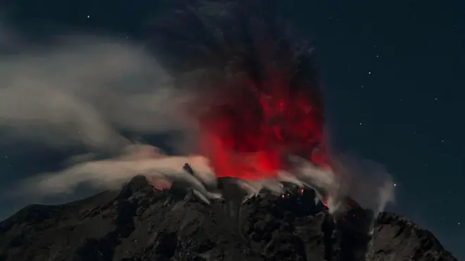 Gunung Sinabung menyemburkan asap kemerahan beserta abu, dilihat dari Kabupaten Karo, Sumatra Utara.