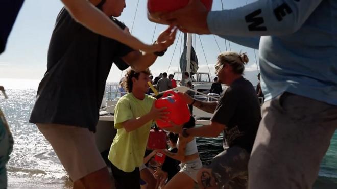 美国夏威夷毛伊岛居民组成人链从志愿者救援船卸下救灾物资（13/8/2023）