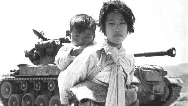 1951లో హీన్‌గ్జు వద్ద యుద్ధ ట్యాంకు సమీపంలో తన సోదరుడిని ఎత్తుకుని వెళుతున్న కొరియన్ బాలిక