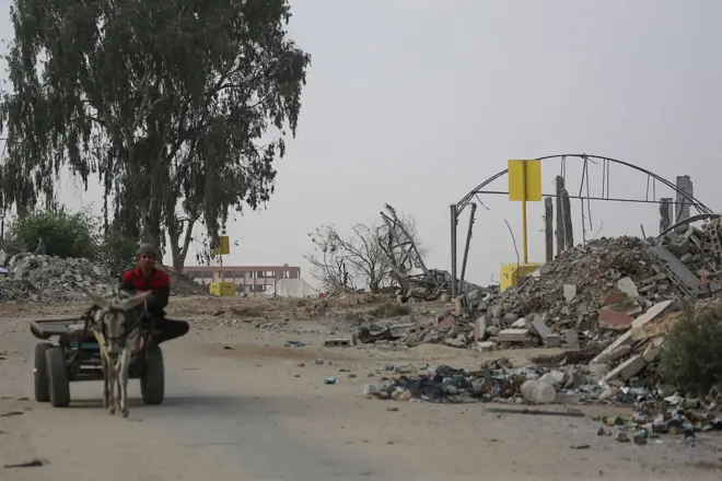 رجل فلسطيني يركب عربة يجرها حمار قرب حاجز خرساني (من الخلف) يُشير إلى "الخط الأصفر"