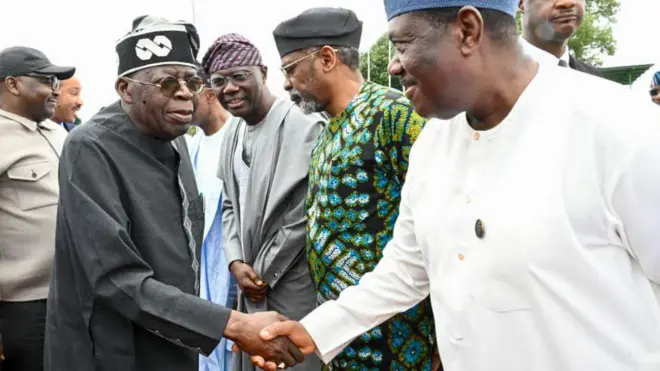 President Bola Tinubu wear all-black cloth dey shake hand SGF wey wear all-white cloth