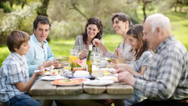 Piknik alanında tahta masa etrafında birlikte yemek yiyen bir aile