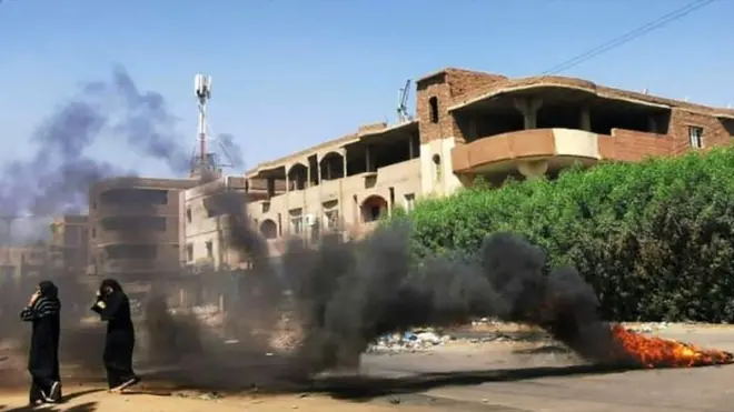 Sudanese women walk in front of tyres set ablaze by anti-coup demonstrators in the capital Khartoum, following calls for civil disobedience to protest last month's military coup, on November 7, 2021.