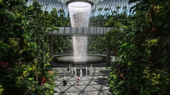 People walk past the Rain Vortex indoor waterfall feature at Jewel Changi Airport in Singapore on August 19, 2021.