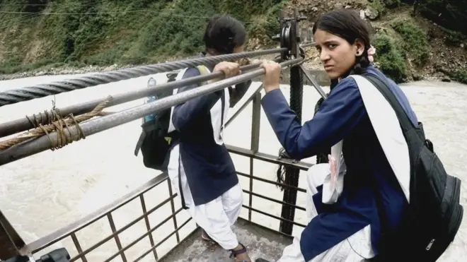 Radhika dan Yoshada melintas sungai deras dalam perjalanan ke sekolah.