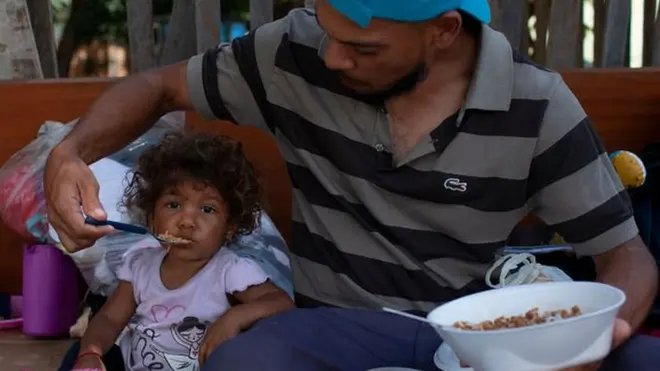 Seorang pria warga Venezuela tengah menyuapi anaknya di salah satu ruas jalan di kota Boa Vista, negara bagian Roraima, Brasil, 23 Agustus 2018.
