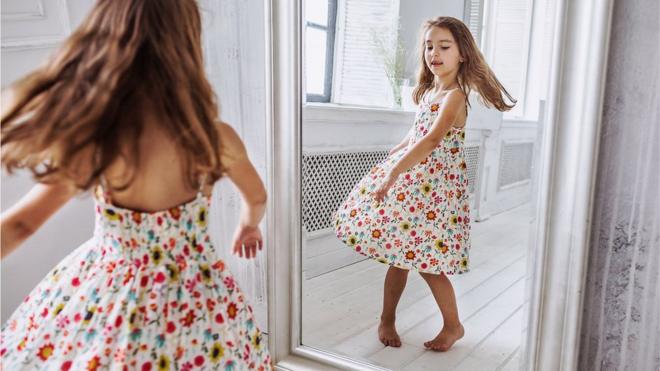 Menina de vestido em frente a espelho