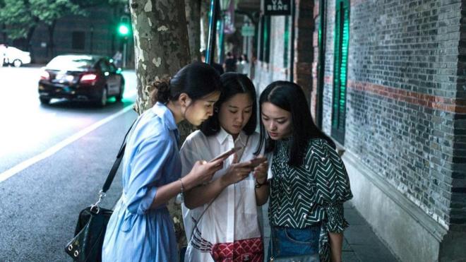 Chinesas observam telefone celular