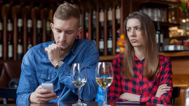 A man on his phone during a meal with his girlfriend