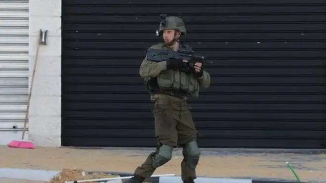 جندي إسرائيلي يمر من أمام المحلات المغلقة في الموقع حيث قتلت قواته ثلاثة فلسطينيين بالرصاص، بالقرب من حاجز صرة العسكري خارج مدينة نابلس بالضفة الغربية، 12 مارس/آذار 2023.