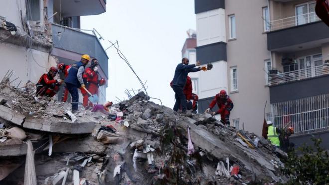 People and rescue workers stand on the rubble of a collapsed building following an earthquake in Adana, Turkey, February 7, 2023.