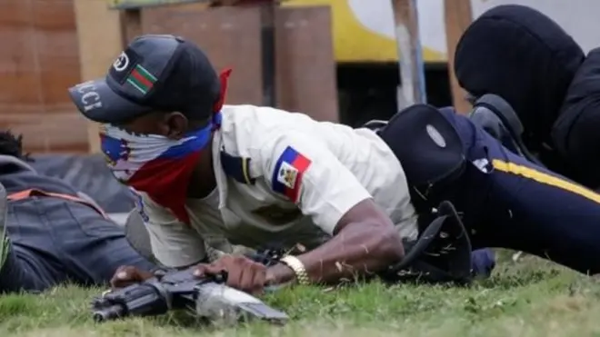 A masked man in a Haitian National Police uniform crawls on the ground during a shooting in Champ de Mars, Port-au-Prince, Haiti February 23, 2020