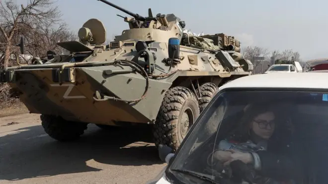 One refugee wait in a car as armoured personnel carrier of pro-Russian troops dey drive out of one checkpoint inside di city of Mariupol